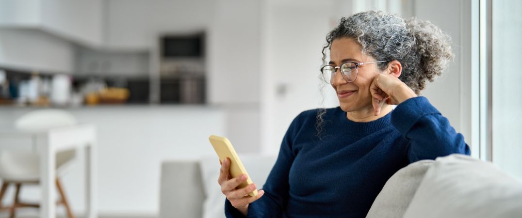 Eine Frau sitzt auf dem Sofa und nutzt ihrt Smartphone